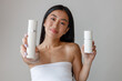 © Friends Stock - Asian young woman holding two bottles of cosmetic cream