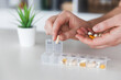 © Lena Ivanova - Female elderly hands sorting pills. Closeup of medical pill box with doses of tablets for daily take a medicine with white, yellow drugs and capsules. Young woman getting her daily vitamins at home.