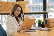 © ArLawKa - Smiling Asian woman looks at boxes and uses laptop to check information in parcel delivery boxes before sending them to customers. Entrepreneurs, small businesses work at home work online marketing