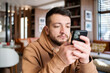 © Julija - Young bearded man is sitting in cafe ,using smartphone. Remote work.Hipster man blogging, chatting, cheking email. Student learning online. Education for adult.