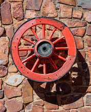 A Red Vintage Wagon Wheel, Mounted On A Rocky Wall.