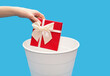 A man throws a gift box into a trash can on a blue background. A human hand holds a red gift box and throws it into a white trash can. Didn't like gift or junk gift concept with free space for text