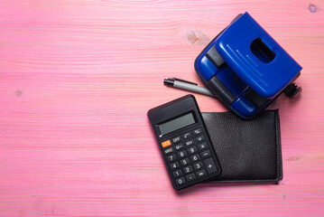 Office table concept background. Stationery, calculator and wallet on the pink background.