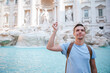 Young man near fountain Fontana di Trevi with coins in hands