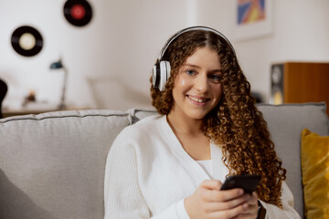 Close-up of the face of a smiling very beautiful brunette with gray eyes. The girl is wearing a white sweater and a white T-shirt. Listens to your favorite music through wireless headphones. Smiles