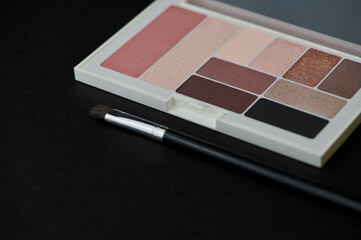 new palette with eye shadow and blush of different colors and a cosmetic brush on black background