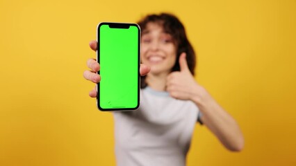 Young woman showing smartphone with green chroma key screen, advertising for your phone. Wow emotion. Attractive young girl on yellow background. High quality 4k footage