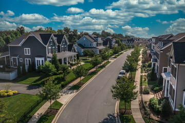 Aerial view of modern upper class suburban American real estate development community, large single family homes with vinyl and brick siding portico leading up to the entrance cloudy blue sky