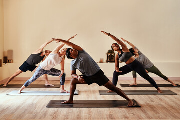 Wall Mural - Yoga lets your inner warrior loose. Shot of a group of young men and women practicing yoga in a fitness class.