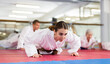 © JackF - Young woman in kimono doing push-ups during group karate training.