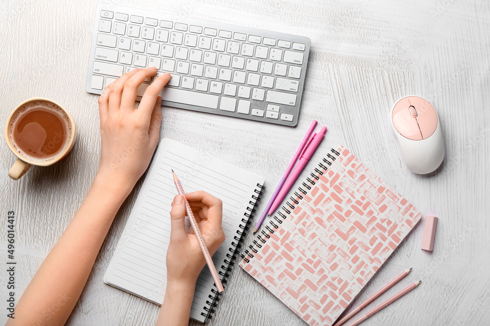 Female hands with blank notebook, keyboard and stationery on light grunge background