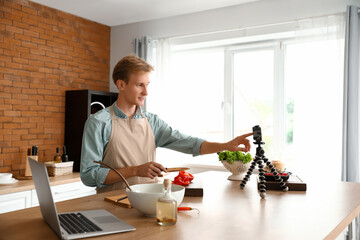 Canvas Print - Young man cutting bell pepper while recording video tutorial in kitchen