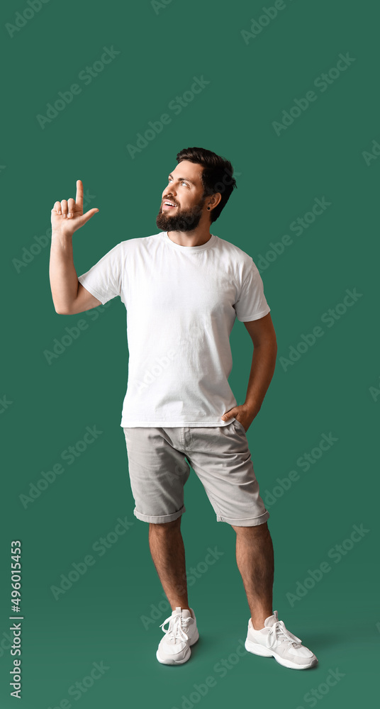 Handsome man in white t-shirt pointing at something on green background