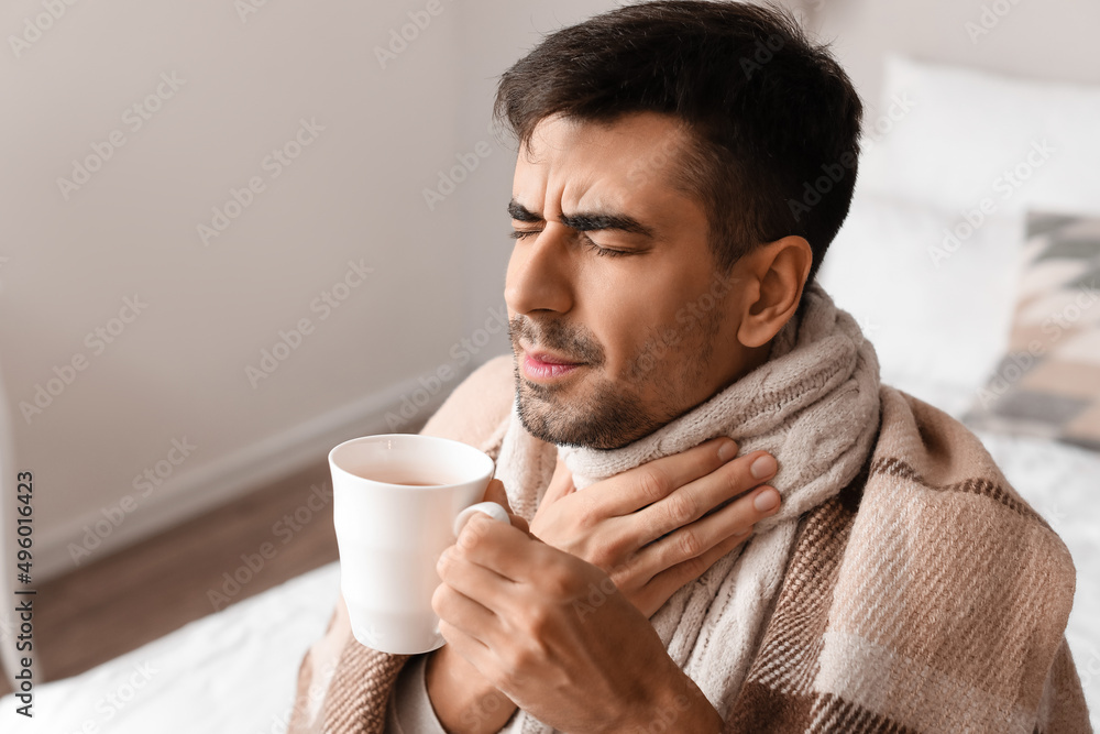 Ill young man with sore throat drinking hot tea at home