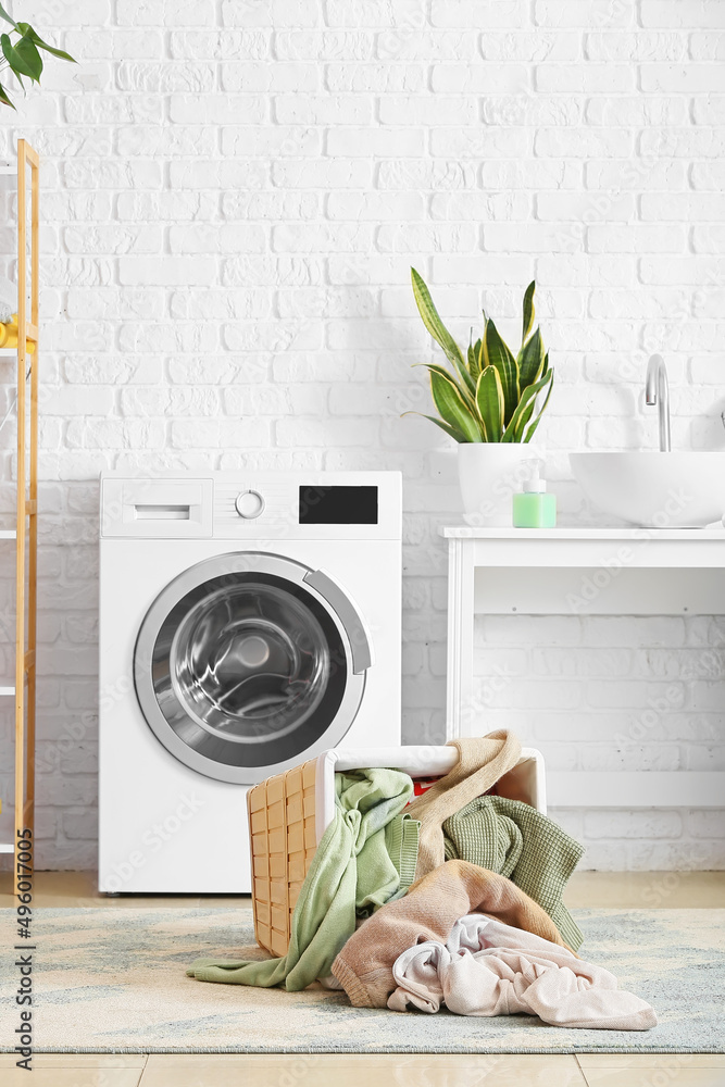 Basket with dirty clothes near washing machine in laundry room