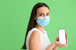 Young woman in mask with applied medical patch and mobile phone on green background