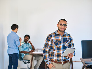 Poster - Smart technology makes management so much simpler. Portrait of a young entrepreneur using a digital tablet at work with his team in the background.
