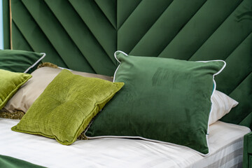 Close up of new green colored bed with decorative pillows, fabric headboard in bedroom in sample model of hotel or apartment