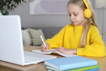 Wall Mural - Cute little girl with modern laptop studying online at home. E-learning