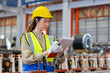 © eakgrungenerd - women engineer take notes on paperwork quality control standing at machine of factory warehouse.