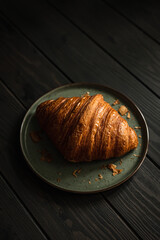 Wall Mural - A freshly baked delicious croissant on a plate on a wooden table, shot in dark and moody style with natural light, selective focus