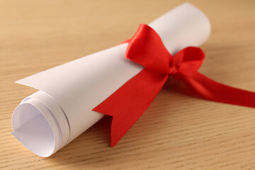 Wall Mural - Graduation diploma tied with red ribbon on wooden table, closeup