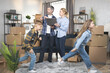 © sofiko14 - Two funny kids, boy and girl, playing, running and having fun during relocation, while focused parents behind using laptop and discussing design at modern appartment.
