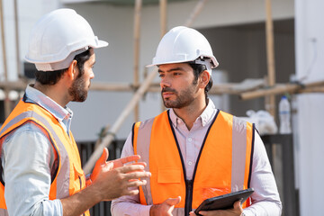 Fototapete - Professional architects in safety vests at a construction site while discussing their work plan at building site.