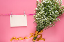 Mockup Of Pastel Pink Card Note Blank Paper Sheet Hang On Rope With Clothes Peg And Spring Fresh White Flower Bouquet Isolated On Pink Background.