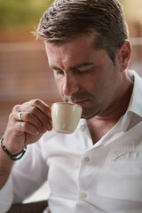 Wall Mural - A senior businessman in casual clothes sits on the terrace of a luxury house and drinks morning coffee. Selective focus 