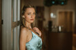Eine junge, blonde Frau mit hellblauen Augen lehnt an einer Restauranttür des Steigenberger Grand Hotels Peterberg. Sie trägt ein Abendkleid in Augenfarbe und wartet sehnsüchtig auf ihre Verabredung. 