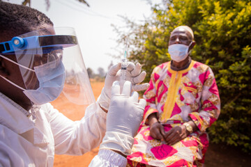 an african doctor prepares a syringe to inject the vaccine into an elderly patient. concept of vacci