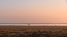 The Pastel Pinks And Blues Glow Above A Lone Surfer At The Water's Edge On Belhaven Bay To The South Of The North Sea