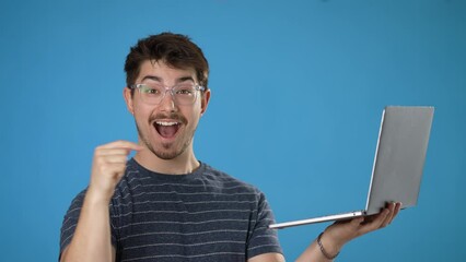 Wall Mural - Young smiling happy man 20s in striped t-shirt hold use work on laptop pc computer browsing chatting surfing internet isolated on plain blue background studio portrait. People lifestyle concept