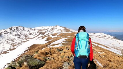 active woman with backpack hiking with scenic view on snow capped mountain peaks of seetaler alps in