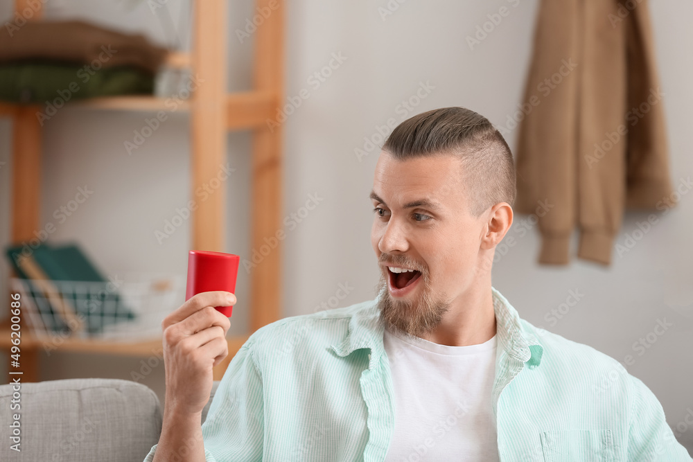 Emotional man holding wireless portable speaker on sofa