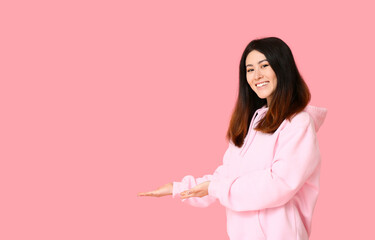 Sticker - Young Asian woman in hoodie showing something on pink background