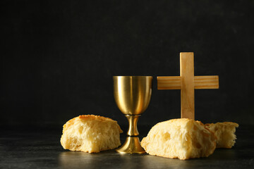 Cup of wine with bread and cross on dark background