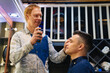 © andrey - the hairdresser styling a brunette man and spraying hairspray in a barbershop