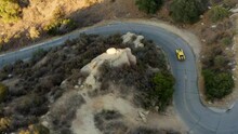 Aerial View Of A Retro Sports Car Turning On A Winding Highland Road - High Angle, Drone Shot