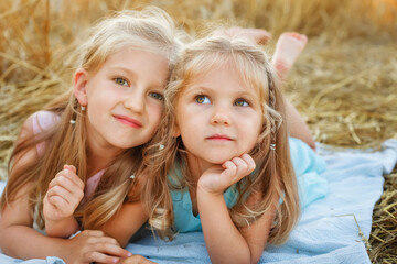 Two girls are lying on a blanket in a wheat field. The sisters are lying on a blanket against the background of rye ears.