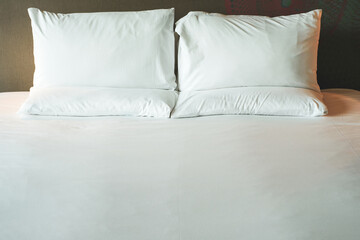 Wall Mural - Clean Bedding sheets and pillow on natural wall room background. White bedding and pillow in hotel room. White pillows on empty bed.