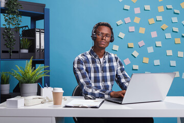 Wall Mural - exhausted helpline support operator sitting in call center workspace while looking at camera. fatigu