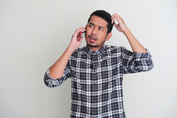 Adult Asian man showing confused expression while talking with someone on the phone