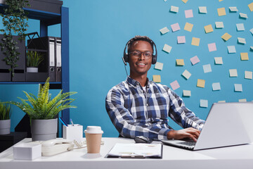 Wall Mural - cheerful smiling customer support consultant wearing headset while in call with company client. joyf