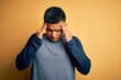 © Fernando - Young handsome latin man wearing casual t-shirt standing over yellow background with hand on head for pain in head because stress. Suffering migraine.
