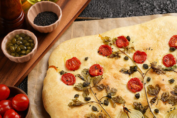 Floral painting focaccia, italian garden flatbread art with parsley, tomatoes, onions, sesame seeds and capers on black structured background