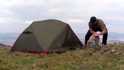 Canvas Print - A strong man moving a large rock from near his wild camping tent in the mountains