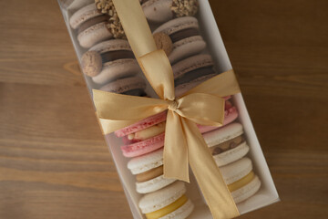 Wall Mural - Sweet dessert macaroons in a box decorated with a ribbon, on a wooden table.