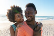 Happy african american woman hugging boyfriend from behind at beach on sunny day